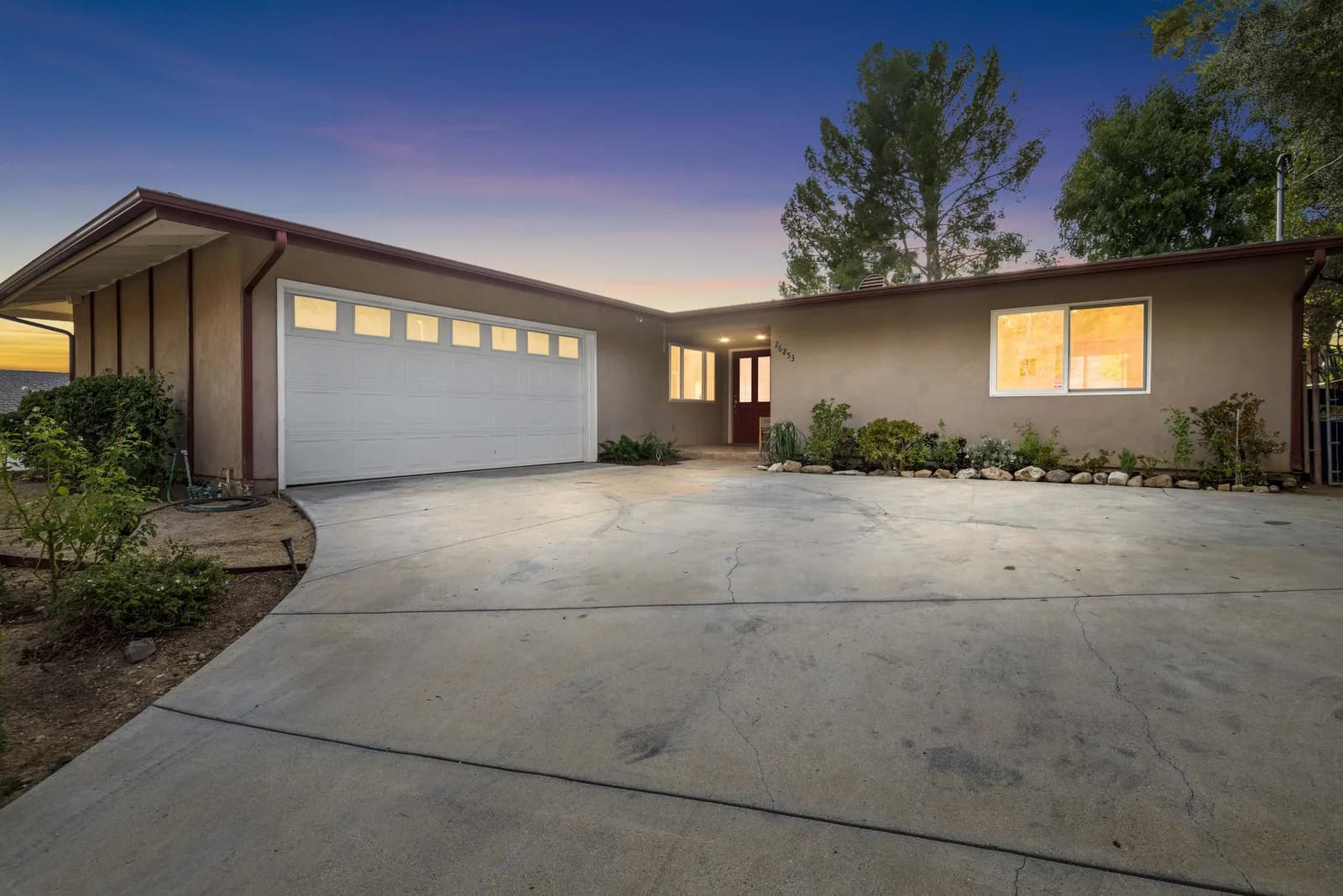Front view of a single-story house with a two-car garage, concrete driveway, and landscaped front yard at sunset