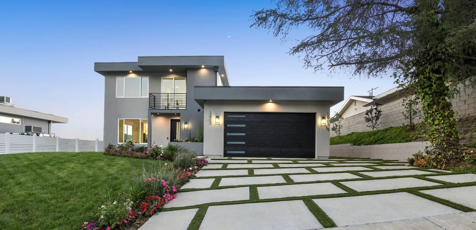 Modern gray two-story house with a black garage door and a front yard with concrete stepping stones
