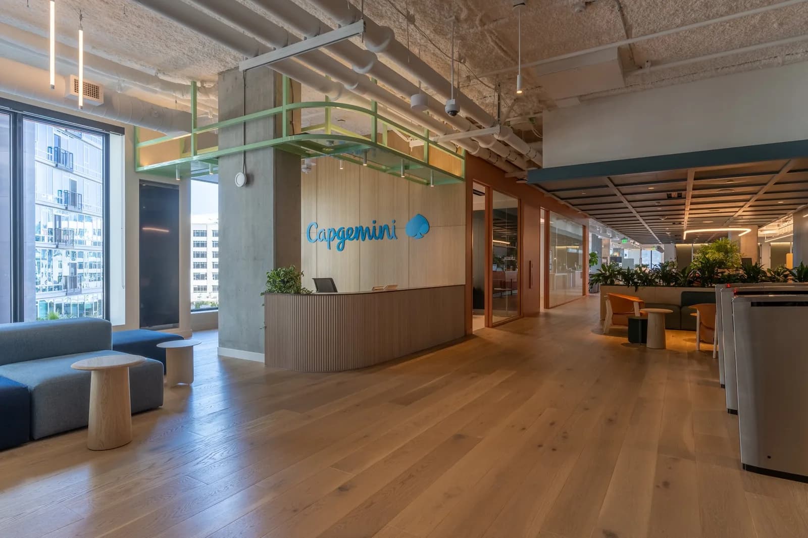 Reception area with Capgemini logo on a wood panel, blue seating, large windows and exposed ceiling