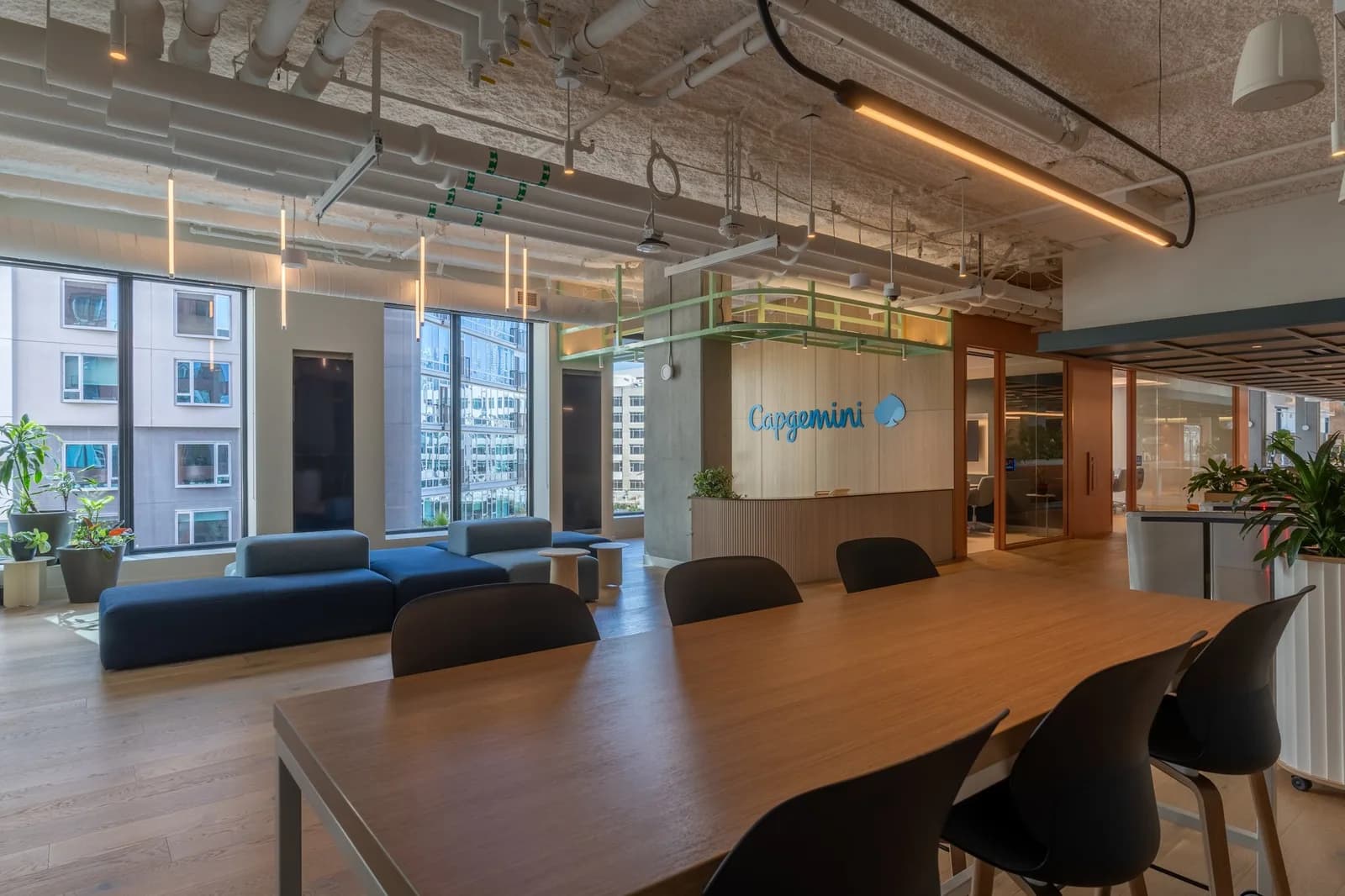 Capgemini reception area with wooden desk, blue seating, large windows, and exposed ceiling pipes
