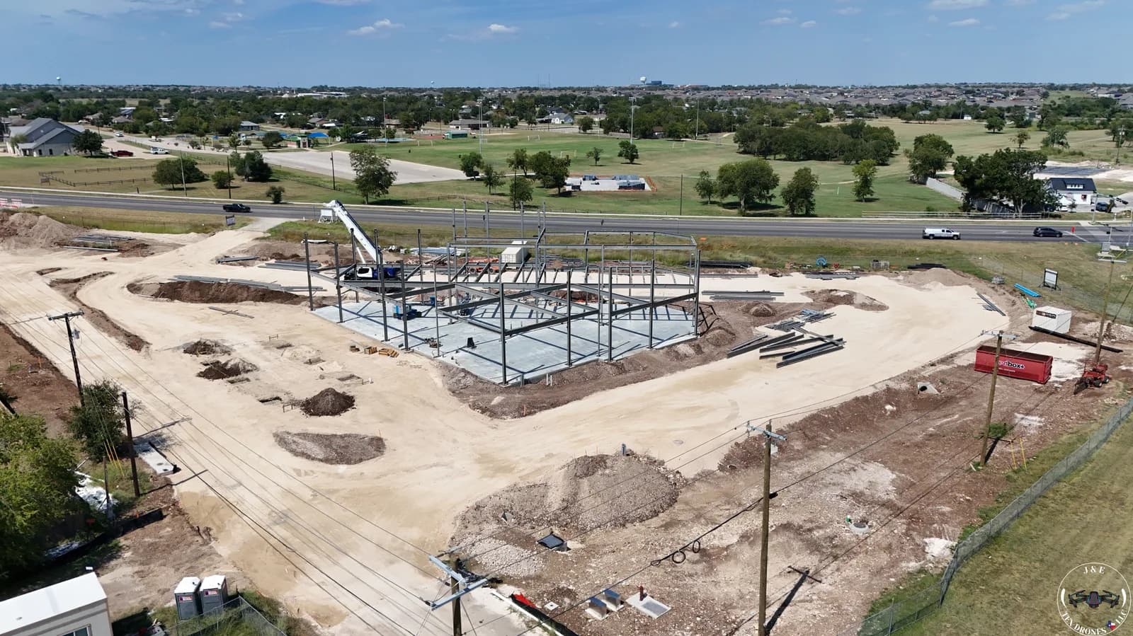 Steel frame structure under construction on a dirt site with a crane and dirt piles