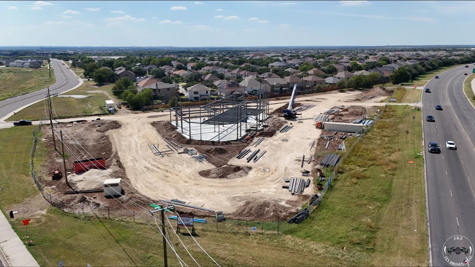 Construction site with steel-framed building, crane, and piles of metal beams near homes