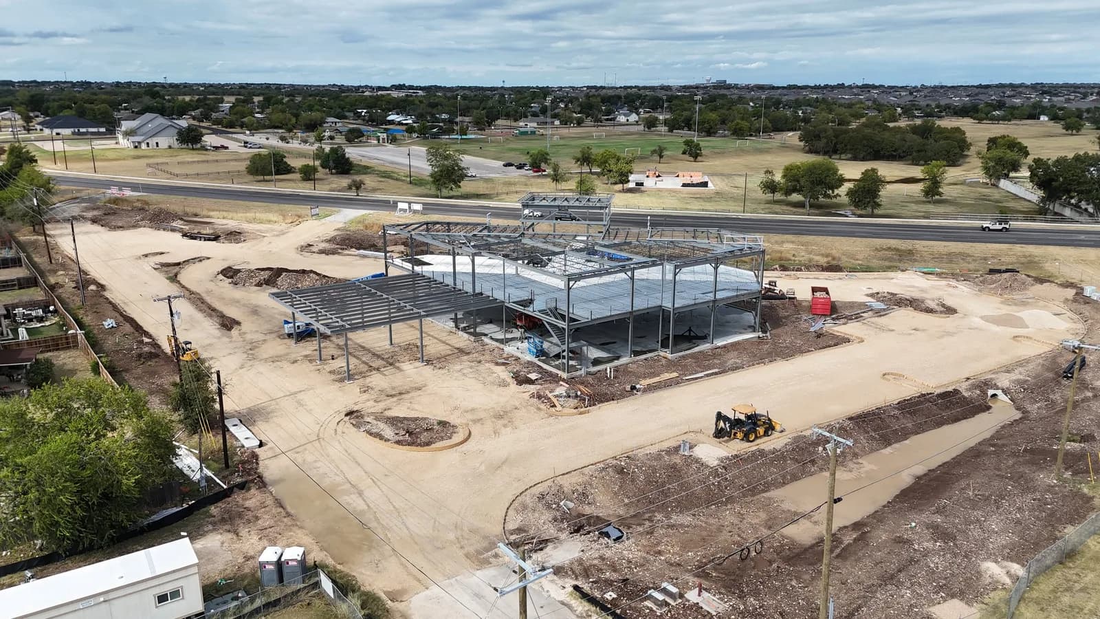 Aerial view of a steel frame construction site with a yellow loader, dirt lots and a nearby road