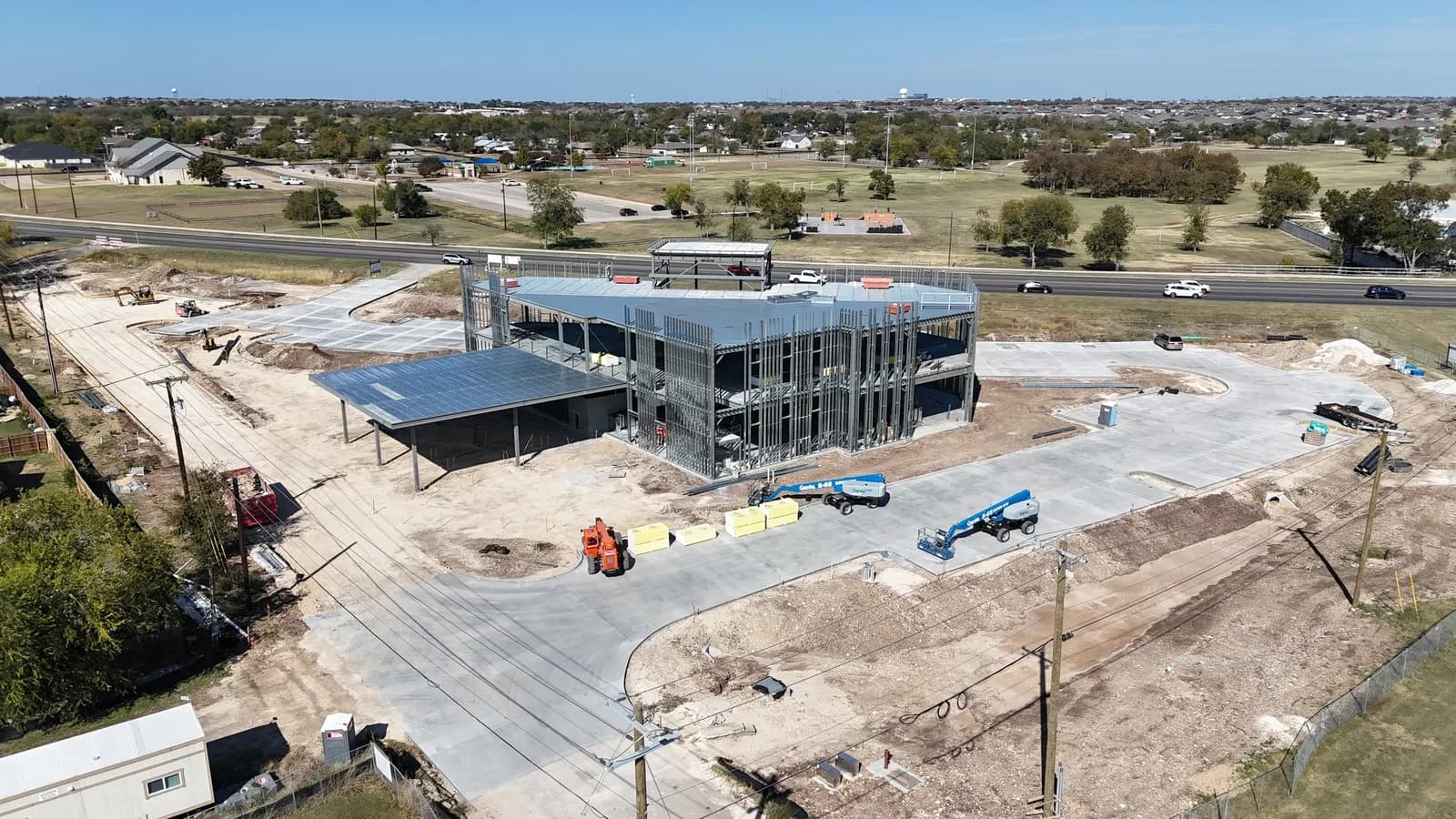 Aerial view of a steel-framed building under construction with equipment and a road in the background