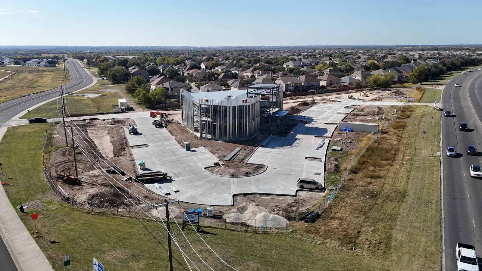 Drone view of a circular steel building under construction with heavy machinery and roads nearby