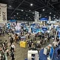 Crowded exhibition hall with booths and attendees, banners hanging overhead