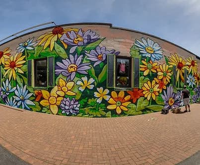 Vibrant floral mural on a curved brick wall with two windows and a person nearby