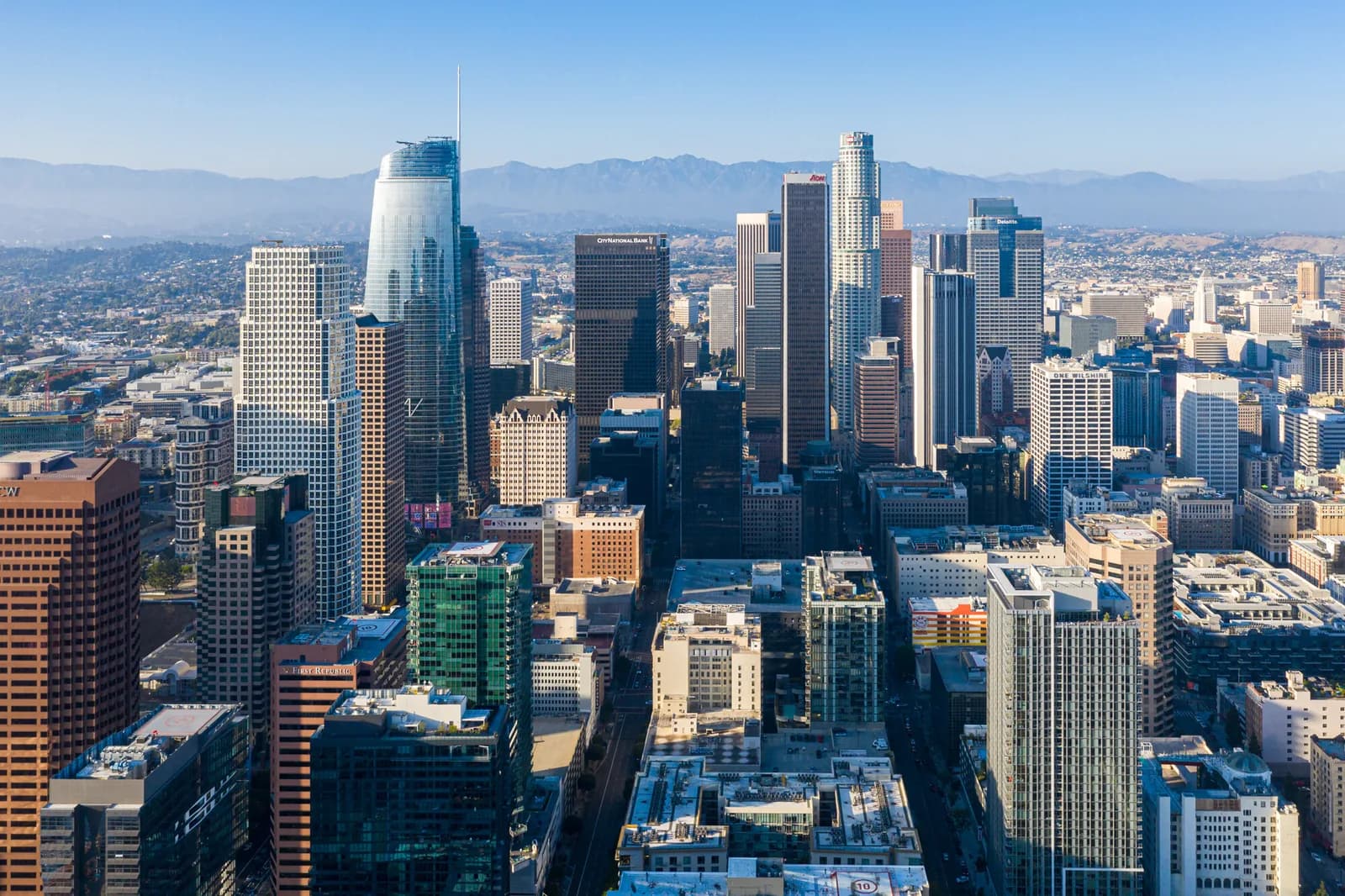 Aerial view of a dense downtown skyline with tall skyscrapers and distant mountains