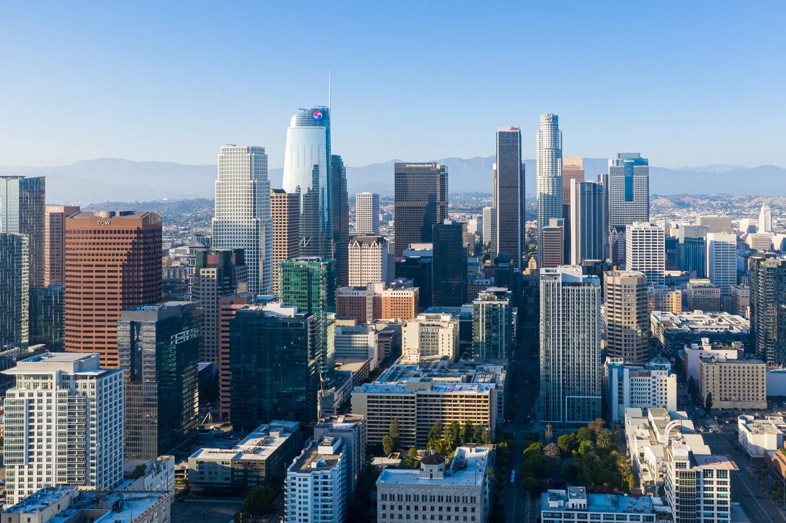 Aerial view of a city skyline with tall skyscrapers under a clear blue sky and distant mountains