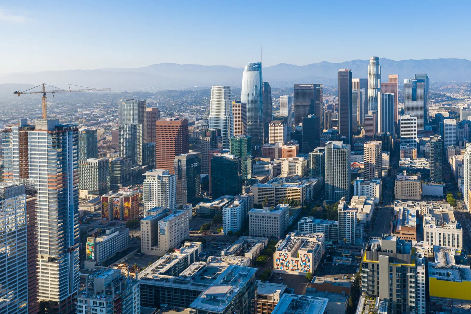 Aerial view of a downtown skyline with high-rise buildings, a crane on the left, and distant mountains
