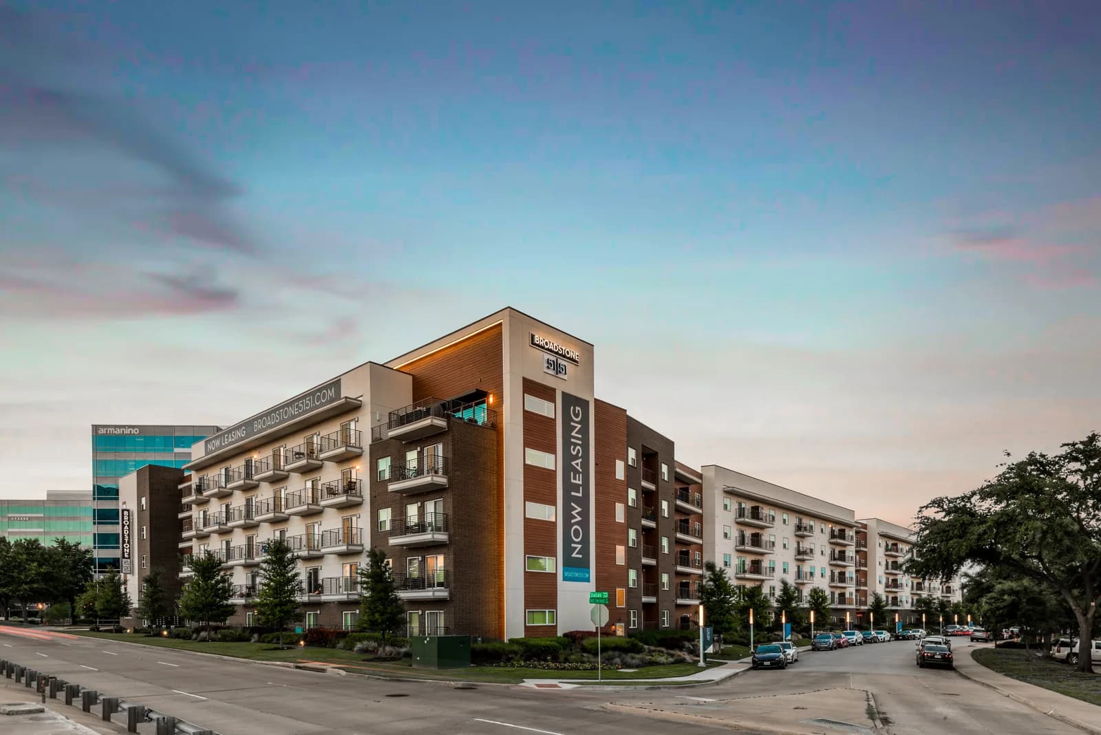 Modern apartment building with balconies and Broadstone now leasing banner, street with cars in foreground