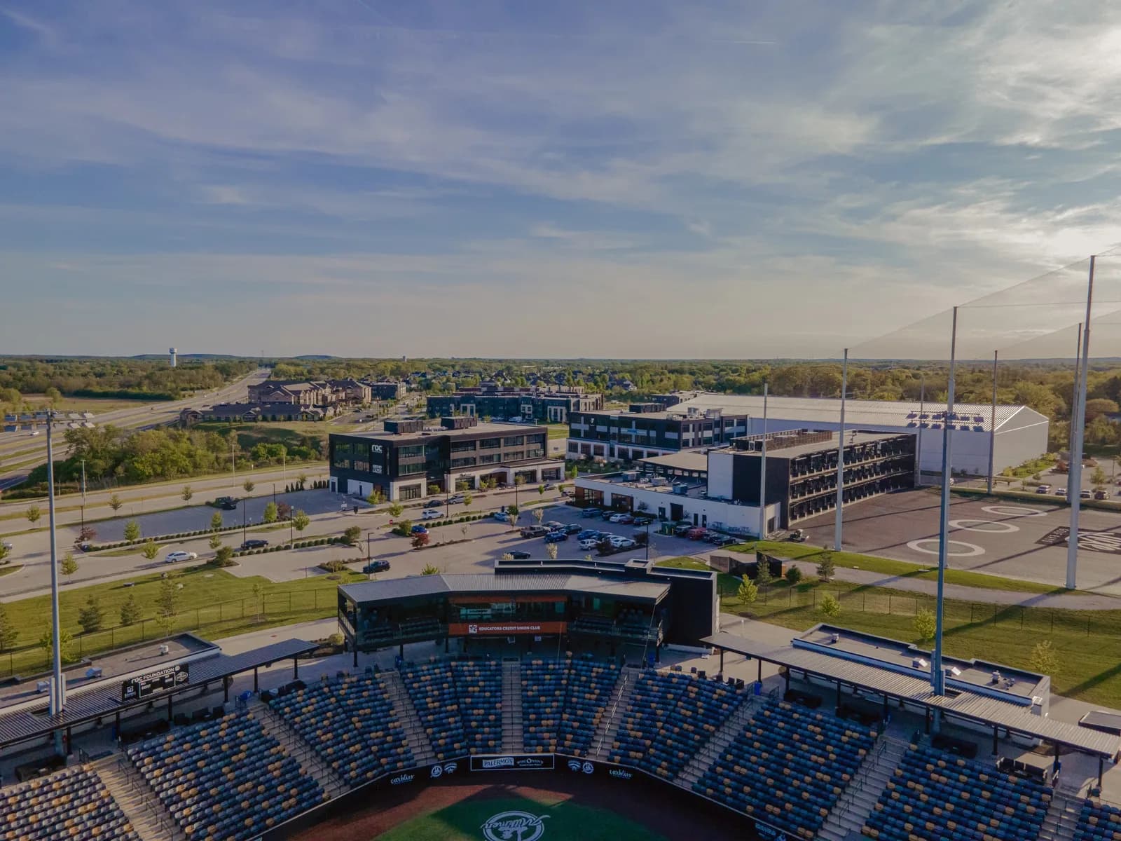 Aerial view of a baseball stadium with blue seats and field, surrounded by modern buildings and parking