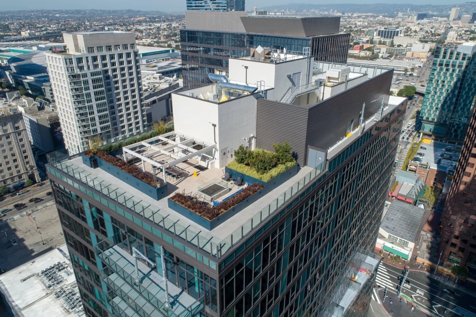 Rooftop terrace on a tall building with planters and seating, overlooking a city skyline