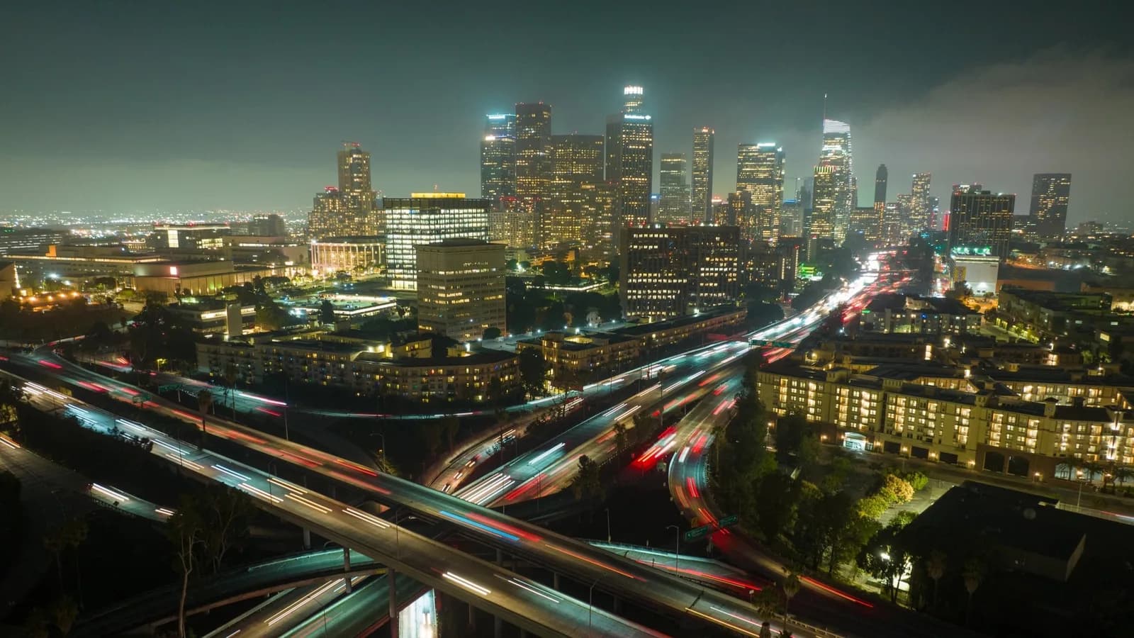 Night city skyline with tall buildings and illuminated windows, plus multi-level highways with light trails