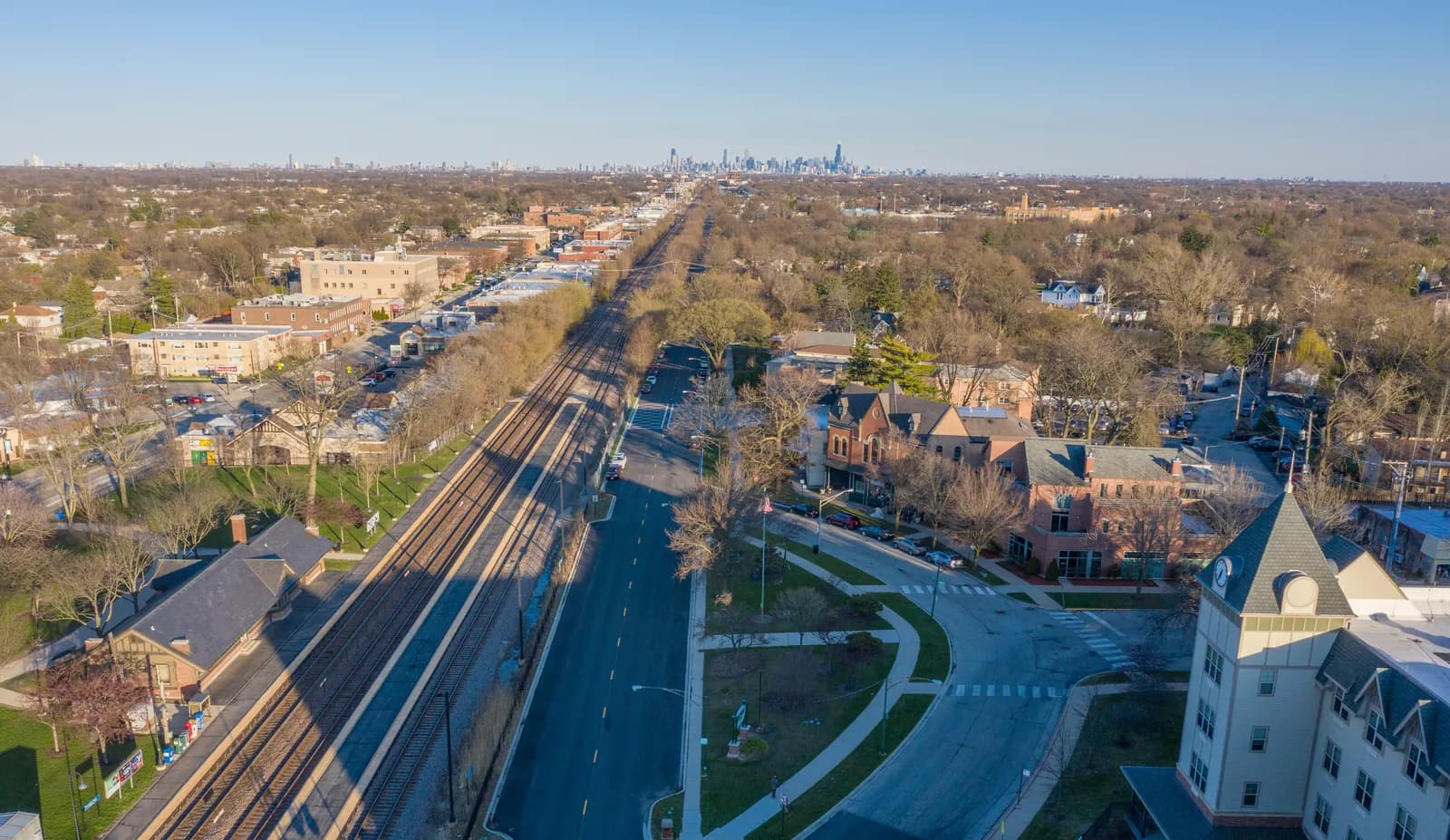 Aerial view of a suburban area with parallel railway tracks, a long road, and a distant city skyline