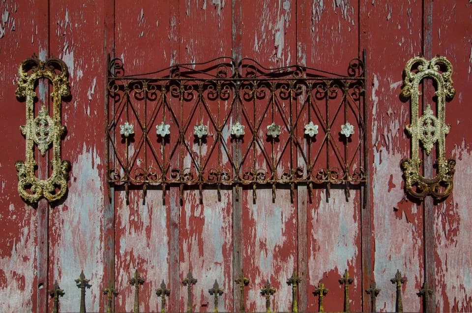 Rusty red wooden door with decorative wrought iron grille and ornate gold handles