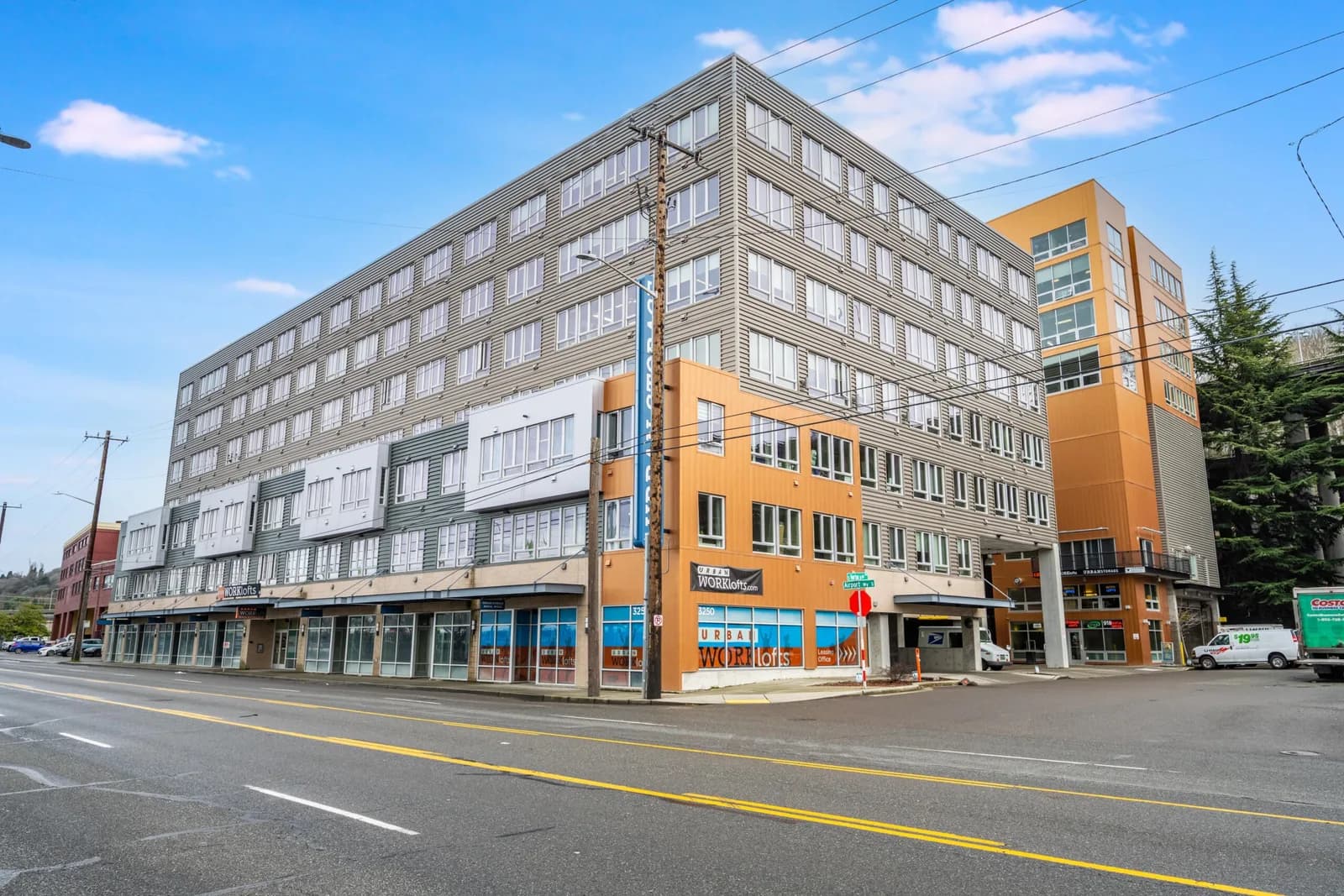 Six-story grey building with many windows and orange accents, street-level shops