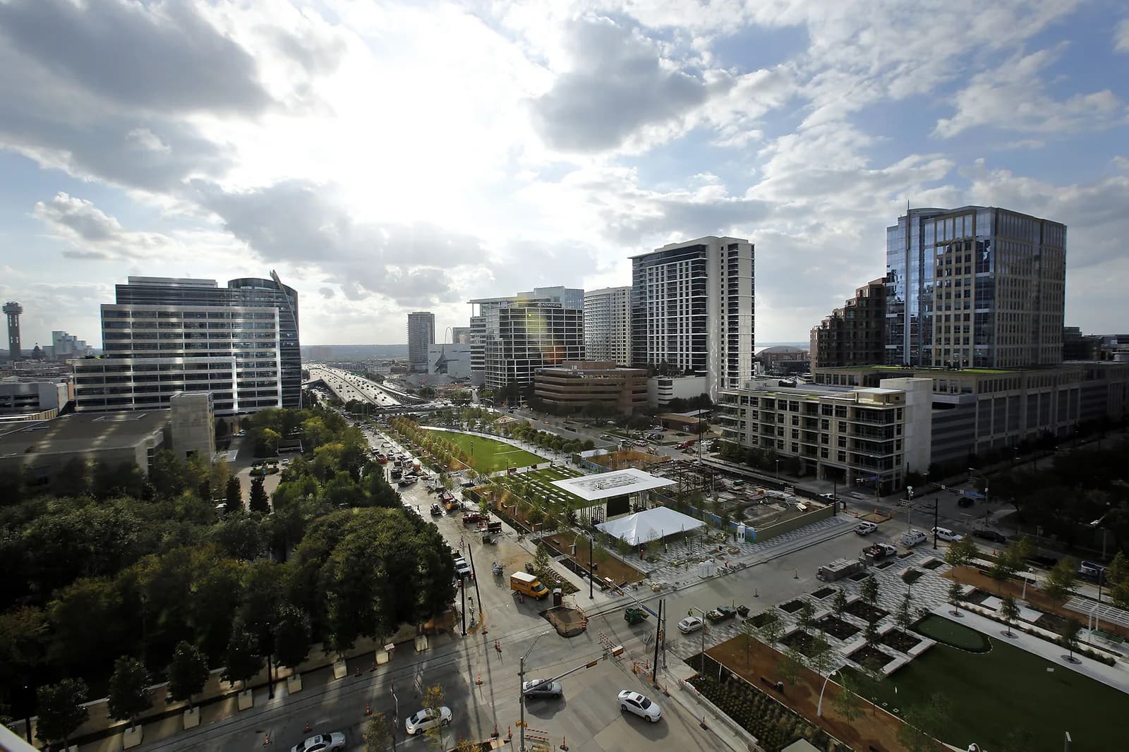 Aerial view of a modern city with glass high-rises, a highway, and a green park