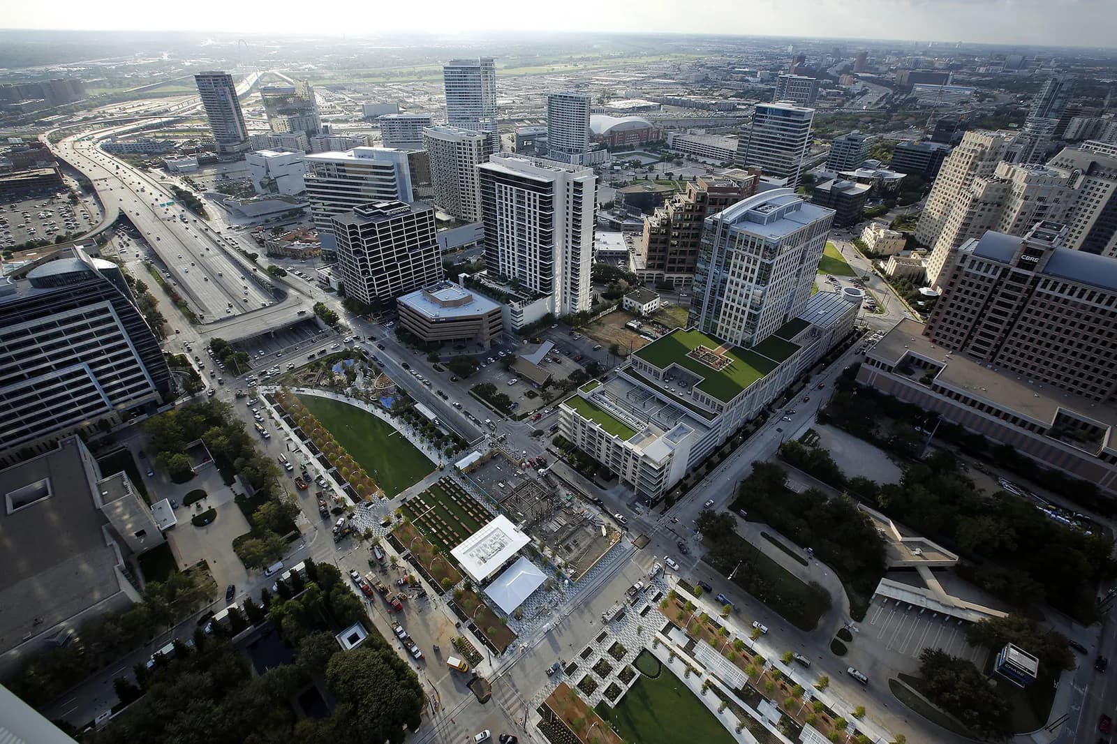 Aerial view of a downtown skyline with tall buildings, a curved elevated highway, and a green park