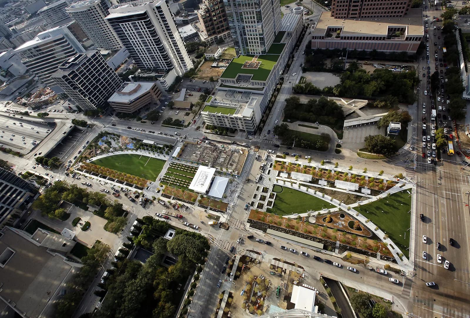 Aerial view of a city block with high-rise towers, roads, and a green rooftop garden area