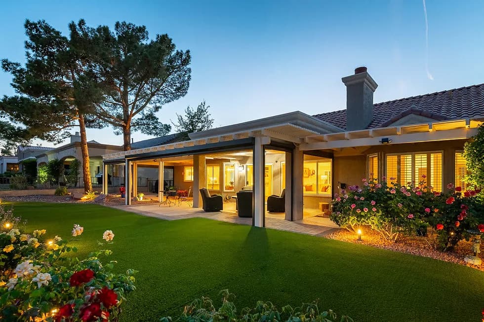 Backyard of a modern house with a covered patio, outdoor seating, lush green lawn, and rose bushes at dusk