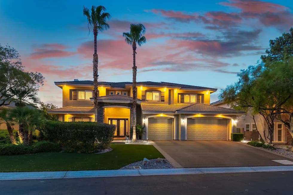 Two-story home with a two-car garage, palm trees, and warm exterior lighting at dusk