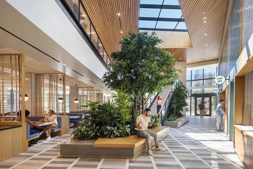 Atrium with a large central tree planter, seating booths, and people using phones