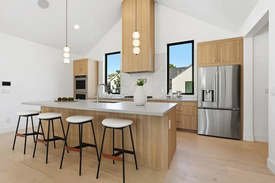 Modern kitchen with wood island, four stools, pendant lights and stainless steel refrigerator