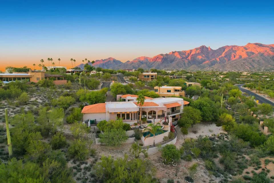 Aerial view of a desert house with pool and surrounding vegetation at sunset with mountains beyond
