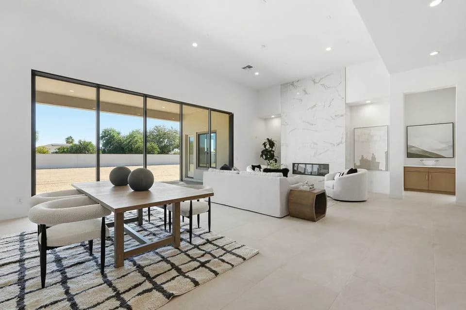 Bright modern living and dining area with large glass doors, white sofa, wooden table, patterned rug