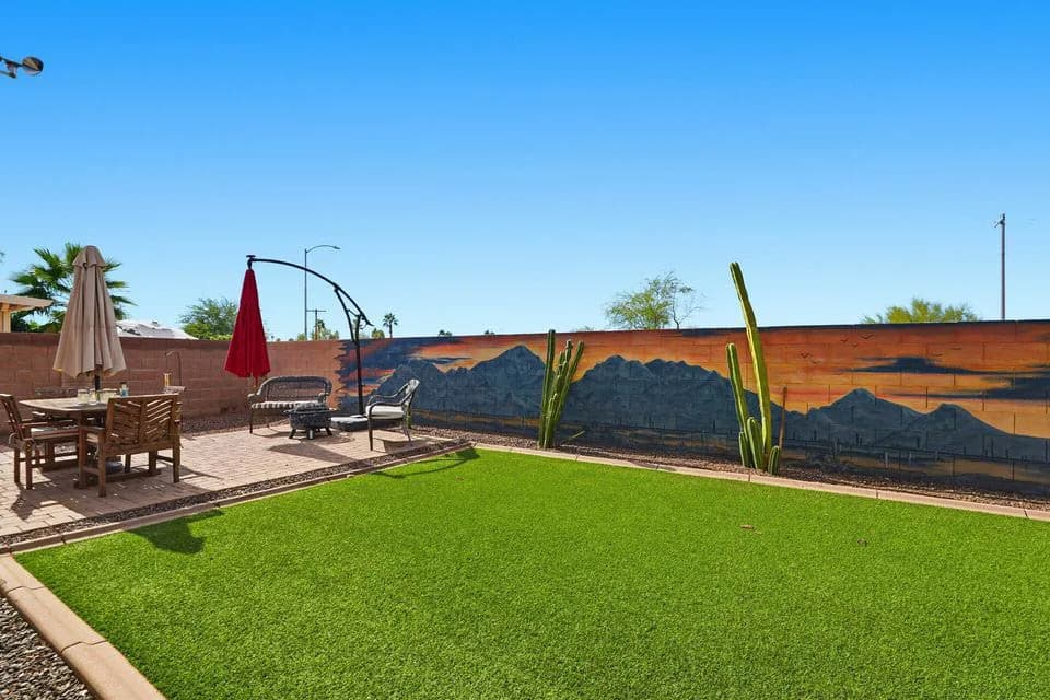 Backyard with artificial turf, patio table and chairs, lounge seating, and painted mountain mural