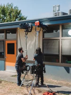 Two technicians in harnesses stand by a rig outside a building, with cables on the ground