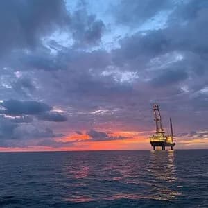 Offshore platform near the horizon at sunset, with dark clouds and calm sea