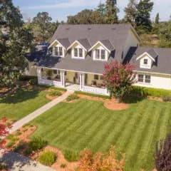Two-story house with dormer windows and a front porch, manicured lawn with mowing stripes and a tree