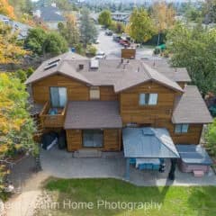 Aerial view of a brown wooden house with multiple roofs, a deck, and surrounding trees