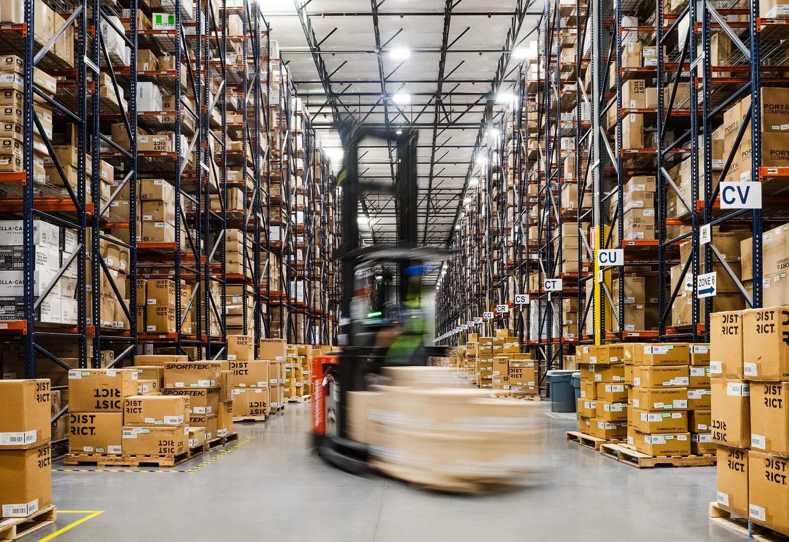 Blurred forklift moving through a tall racked warehouse filled with stacked cardboard boxes