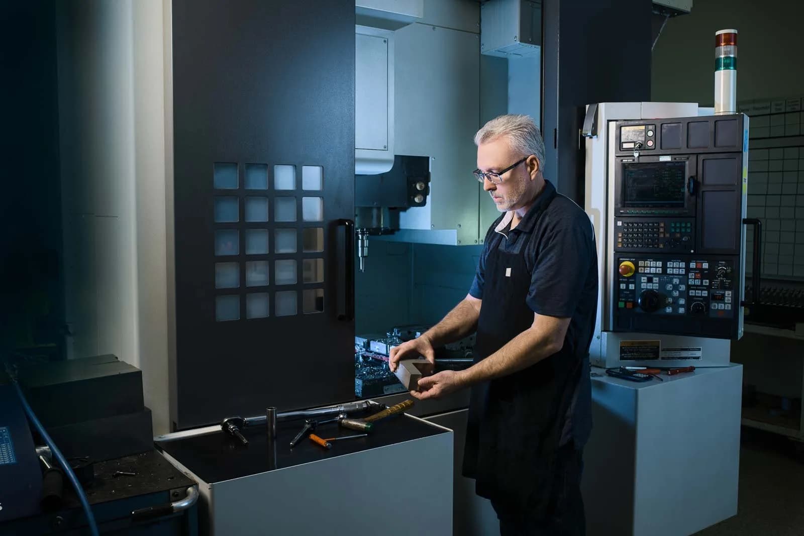 Man inspecting a metal part beside a CNC milling machine in a workshop
