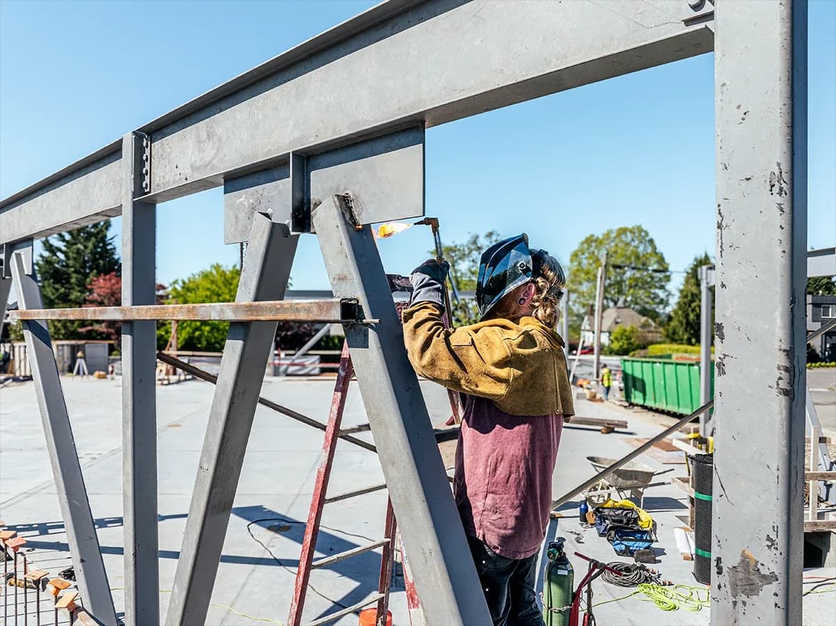 Welder wearing protective gear welding a steel beam on a metal frame at a construction site