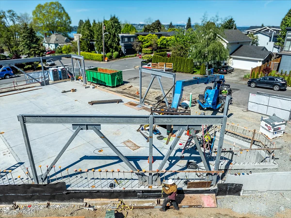 Aerial view of a construction site with steel frame, concrete foundation, blue equipment and a worker