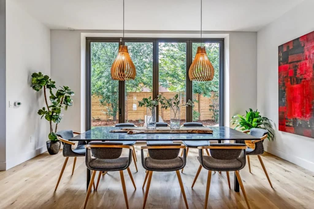 Modern dining room with a glass table, woven pendant lights, chairs, plants, and a red painting