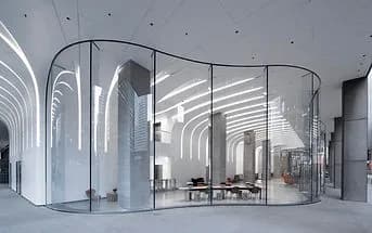Curved glass wall enclosure with modern conference tables and chairs inside a bright interior