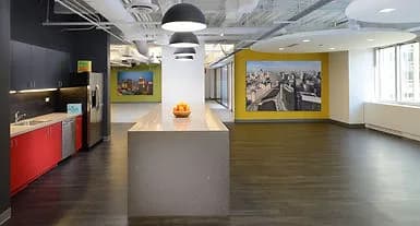 Open office kitchen with island, dark floor, red cabinets, and a yellow accent wall with photos