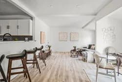 Open plan living room with a kitchen island, bar stools, dining area and seating on light wood floors