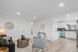 Open living space with white walls, light wood floor, sofa, gray chair, round coffee table, and kitchen