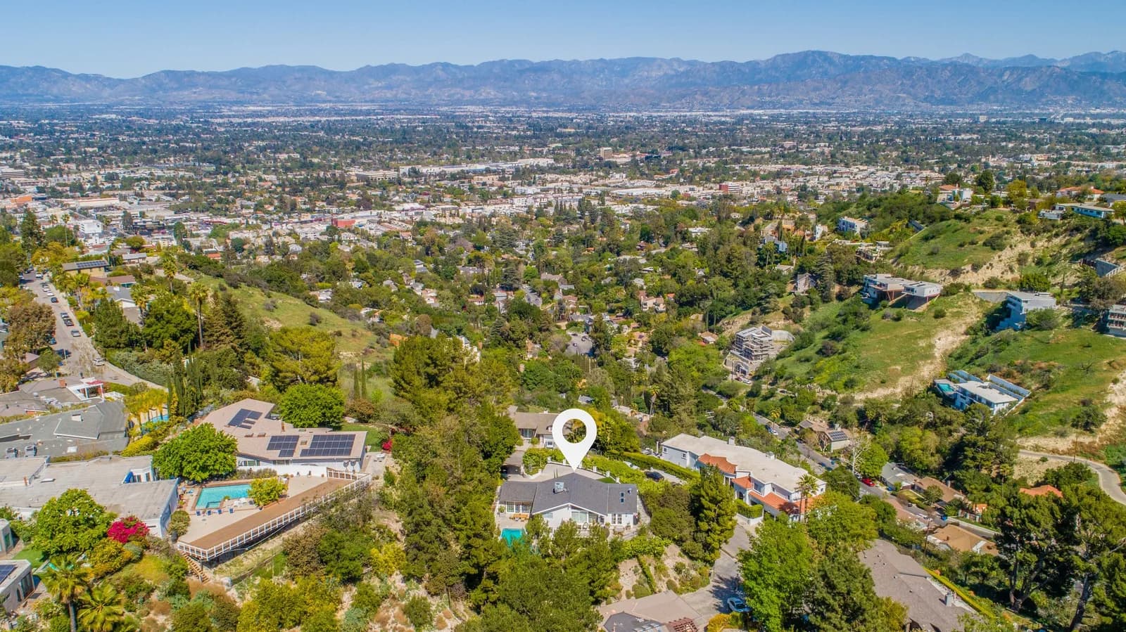 Aerial view of a hillside suburban neighborhood with trees and houses, a map pin on a home