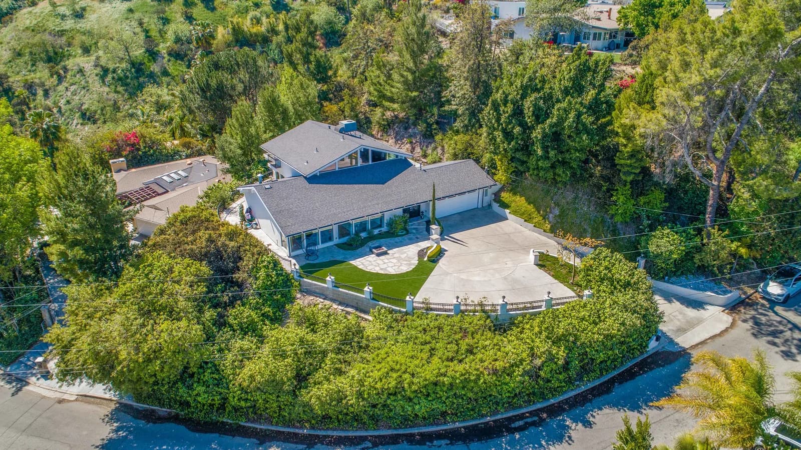 Aerial view of a modern single-family home with a curved driveway, surrounded by trees and a manicured yard