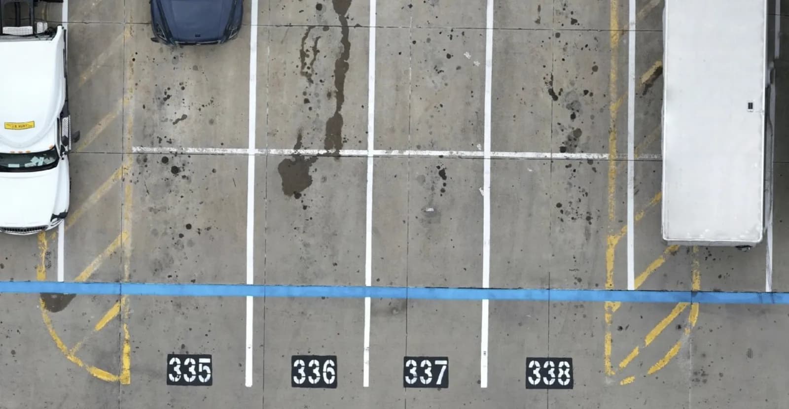 Overhead parking lot with spaces 335–338, white van left and white box truck right, blue line across