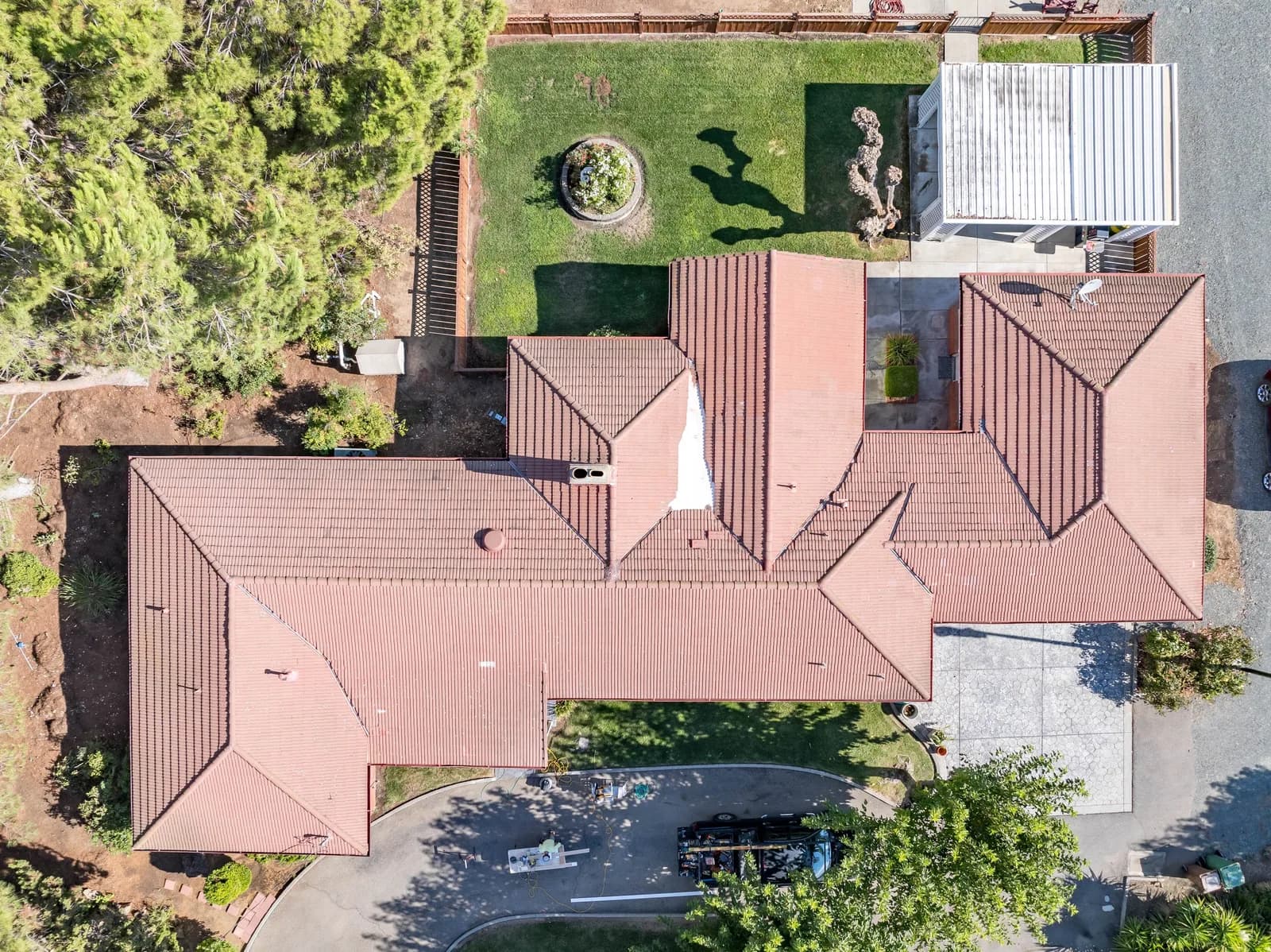 Aerial view of a house with a red-tiled roof, a circular planter in a green yard, and surrounding trees