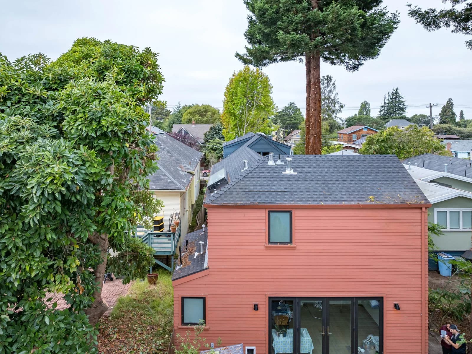 Aerial view of a pinkish-red house with a slate roof, surrounded by trees and neighboring homes