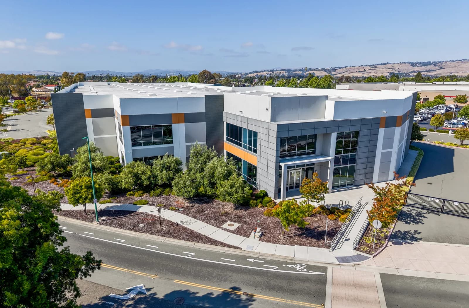 Aerial view of a modern office building with glass windows, gray panels, and orange accents amid landscaping